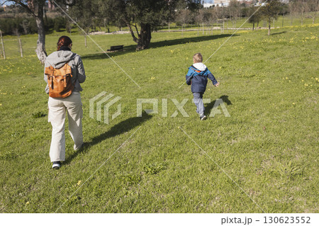 Mother and son walking in green meadow on sunny day 130623552