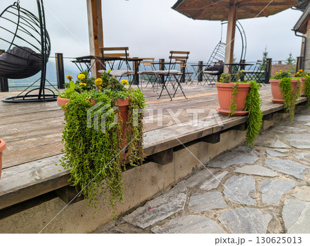 Outdoor terrace with wooden floor, flowerpots and chairs. Cozy atmosphere in the mountains, relaxation and tourism. 130625013