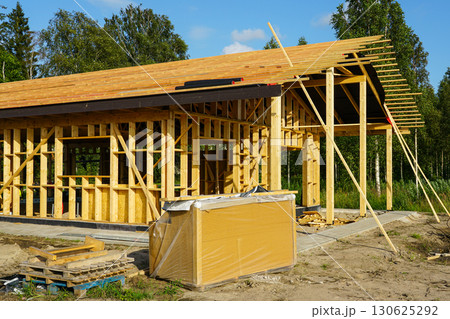 Wooden house frame construction with roof installation on ICF foundation at sunny building site 130625292