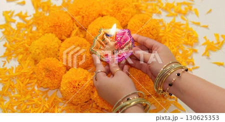 Diwali Celebration. Hands holding traditional diya surrounded by marigold flowers. Diwali Celebration. Hands holding traditional diya surrounded by marigold flowers. 130625353