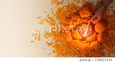 Diwali Festival. Hands lighting a decorative lamp surrounded by marigold flowers. 130625414