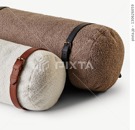 Two fluffy bolster cushions with leather straps resting on white surface 130626059