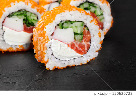 Close-up of tempting california rolls sprinkled with orange tobiko, filled with fresh salmon, cucumber, surimi and cheese, presented on a dark slate plate 130626722