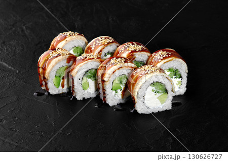 Sushi rolls with eel, avocado, cream cheese, sesame seeds and unagi sauce on black background Sushi rolls with eel, avocado, cream cheese, sesame seeds and unagi sauce on black background 130626727