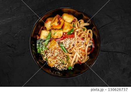 Udon noodles with fried tofu, vegetables and sesame seeds in black bowl 130626737
