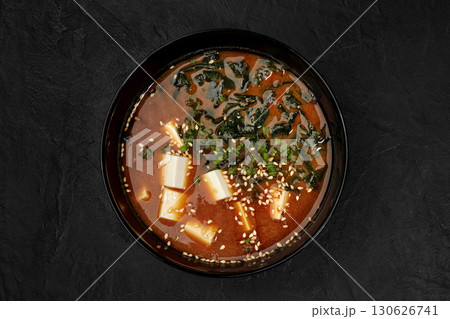 Miso soup with tofu, wakame seaweed, and sesame seeds in black bowl on dark background 130626741