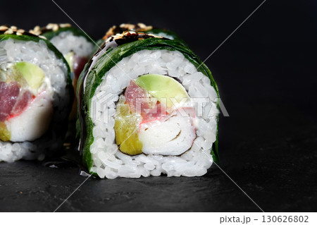 Delicious uramaki sushi rolls with tuna, avocado, surimi and cucumber filling covered with sesame seeds on black background 130626802