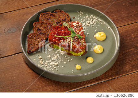 Salmon tartare with avocado, rye bread and drops of sauce garnishing a plate Salmon tartare with avocado, rye bread and drops of sauce garnishing a plate 130626880