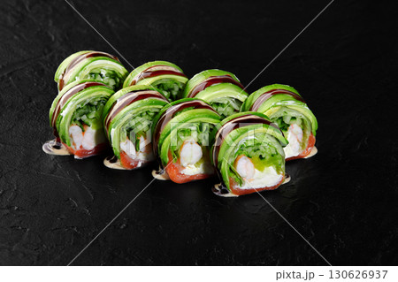 Green dragon sushi rolls with avocado, salmon, and cream cheese drizzled with unagi sauce on dark background 130626937