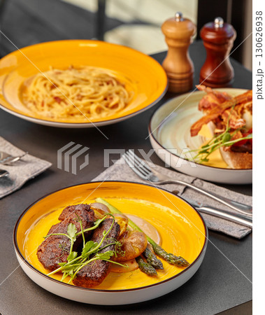 Delicious dishes served on vibrant yellow plates: meat, pasta, and eggs benedict 130626938