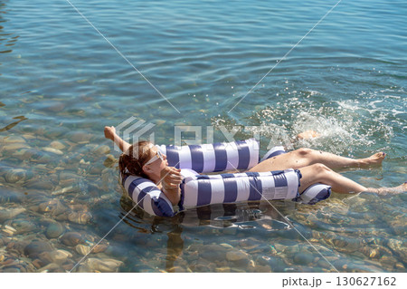 Woman floating water, a woman relaxing on a striped inflatable float in clear blue water, enjoying a peaceful summer vacation day. Woman floating water, a woman relaxing on a striped inflatable float in clear blue water, enjoying a peaceful summer vacation day. 130627162