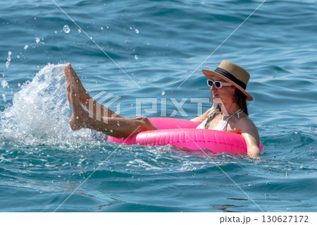 Woman splashing ocean: Relaxed woman on pink float kicking legs, creating water splashes in blue sea for fun. 130627172