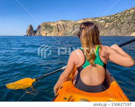 Kayaking, Sea, Cliffs - Woman kayaking near rocky cliffs on a sunny day in the sea. Kayaking, Sea, Cliffs - Woman kayaking near rocky cliffs on a sunny day in the sea. 130627197