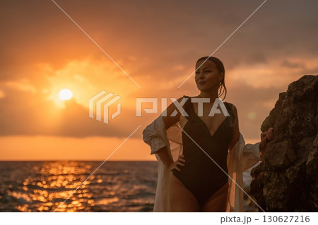 Woman Sunset Beach Rocky Coastline - Enjoying a scenic sunset by the ocean, a woman stands on a rocky coastline. 130627216