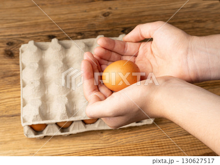 Hand Holding Raw Chicken Eggs Above Wooden Table Background, Taking Brown Eco Bio Egg Hand Holding Raw Chicken Eggs Above Wooden Table Background, Taking Brown Eco Bio Egg 130627517