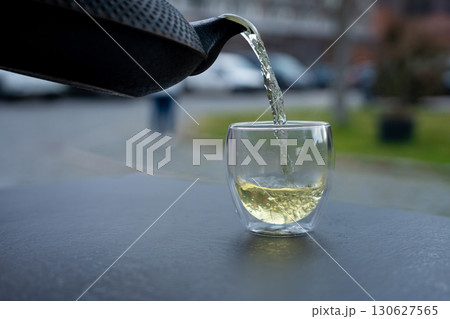 Pouring green tea into a glass from a metal kettle on blurred background, hot drink in teapot 130627565