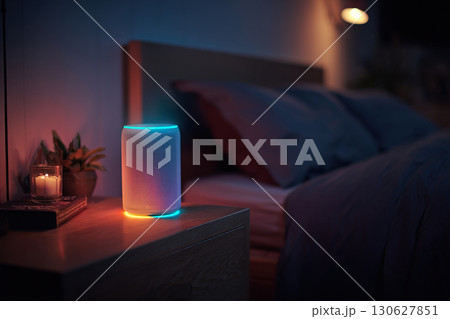 A wireless smart speaker with backlight stands on the bedside table in the evening. 130627851