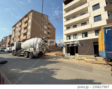Concrete mixer truck parked near modern apartment construction site. Urban development, industrial process and housing infrastructure with engineering work and material transportation. 130627967