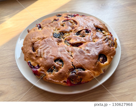 Homemade plum pie served on white plate with wooden background. Dessert preparation, bakery tradition and culinary lifestyle with sweetness, indulgence and food enjoyment. 130627968