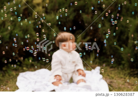 Adorable Baby Boy Playing with Bubbles Outdoors: Soft Focus, Green Garden, Caucasian Child, White Clothing, Joyful Moment, Natural Light Photography. 130628387
