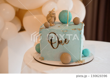 Pastel Blue First Birthday Cake with Teddy Bear Topper, 'One' Lettering, Balloons, and Gold Accents - Celebration Theme. Pastel Blue First Birthday Cake with Teddy Bear Topper, 'One' Lettering, Balloons, and Gold Accents - Celebration Theme. 130628396