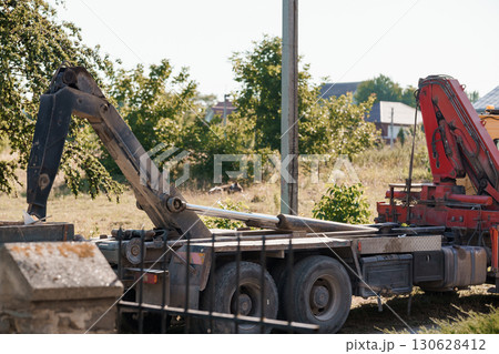 Red Crane Truck Loading Timber on Rural Roadside, Construction Scene, Sunny Day, Green Trees, Orange Machinery, Industrial Equipment, Exterior Shot. 130628412