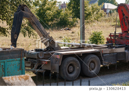 Construction Vehicle with Crane Unloading Materials on Grassy Field, Red and Green Industrial Scene 130628413