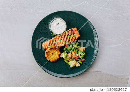 Grilled salmon fillet with vegetables, lemon and creamy sauce on elegant dark plate 130628437