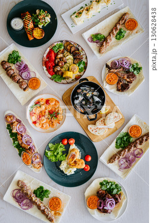 Top view of assorted grilled meats, seafood, and side dishes on a restaurant table 130628438