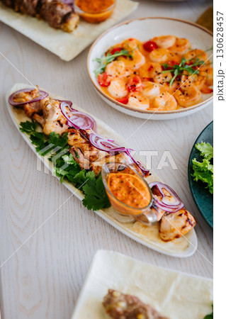 Grilled chicken kebab with red onion, cilantro and spicy sauce on a white wooden table Grilled chicken kebab with red onion, cilantro and spicy sauce on a white wooden table 130628457