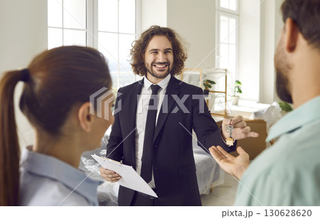 Young male realtor giving house key from new apartments to a happy smiling couple customers. 130628620