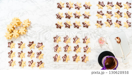 A complete overhead view of decorated snowflake sugar cookies arranged in rows, surrounded by melted chocolate and crushed peppermint, presenting a finished look for the holiday treats. 130628938