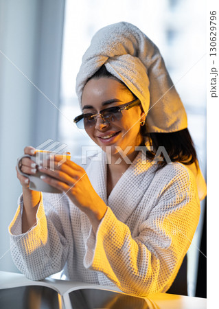 young girl sits comfortably in bright kitchen after her shower wearing glasses and towel on her head savoring warm drink dawn light fills the room.. young girl sits comfortably in bright kitchen after her shower wearing glasses and towel on her head savoring warm drink dawn light fills the room.. 130629796