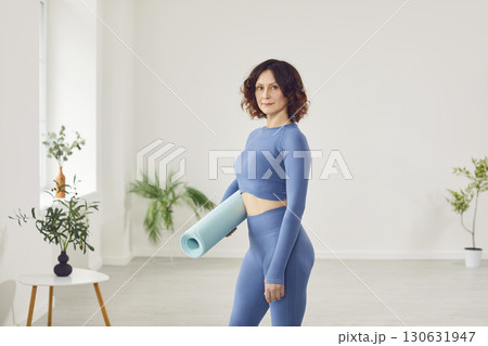 Portrait of sporty attractive woman wearing elegant sportswear holding blue yoga or fitness mat Portrait of sporty attractive woman wearing elegant sportswear holding blue yoga or fitness mat 130631947