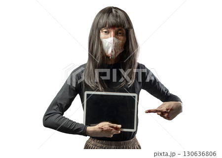 Indonesian southeast asian transgender man dressed as a woman wearing a bloody face mask and showing a tablet screen isolated over a white background. Copy space. Concept of Halloween, Sister Hong, or Indonesian southeast asian transgender man dressed as a woman wearing a bloody face mask and showing a tablet screen isolated over a white background. Copy space. Concept of Halloween, Sister Hong, or 130636806