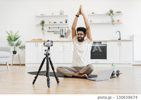 Young adult man practicing meditation, recording wellness video content in serene kitchen environment. Promotes healthy lifestyle, mindfulness exercise, and content creation for online teaching Young adult man practicing meditation, recording wellness video content in serene kitchen environment. Promotes healthy lifestyle, mindfulness exercise, and content creation for online teaching 130638674