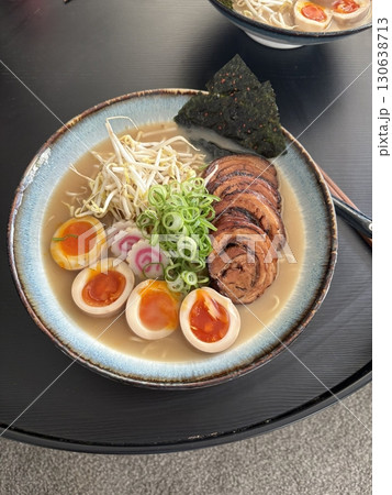 A steaming bowl of ramen with rich broth, tender noodles, sliced pork, boiled egg, nori, and fresh green onions. A comforting and flavorful Japanese classic. 130638713