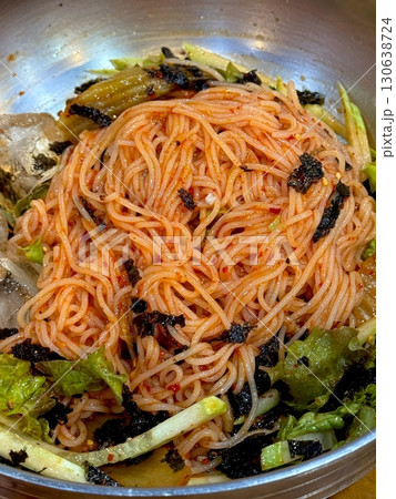 Bibimyeon, a flavorful Korean dish featuring cold noodles tossed in a spicy, tangy sauce, topped with fresh vegetables and a boiled egg. Perfect for summer meals, showcasing vibrant flavors and colors 130638724