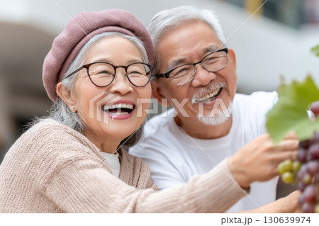 Happy senior couple smiling and enjoying grape harvesting together, holding a bunch of grapes in an outdoor setting, dressed warmly and sharing a joyful moment Happy senior couple smiling and enjoying grape harvesting together, holding a bunch of grapes in an outdoor setting, dressed warmly and sharing a joyful moment 130639974