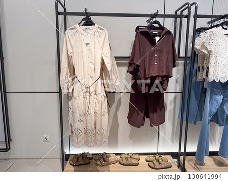 Two outfits, one beige and one brown, are displayed with shoes in a retail store section. Clothing trade, fashion commerce, consumer shopping and textile industry within urban lifestyle culture. Two outfits, one beige and one brown, are displayed with shoes in a retail store section. Clothing trade, fashion commerce, consumer shopping and textile industry within urban lifestyle culture. 130641994