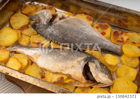 Dorado fish on a baking sheet with potatoes. Whole roasted seabream, gilt-head bream Dorado fish on a baking sheet with potatoes. Whole roasted seabream, gilt-head bream 130642371