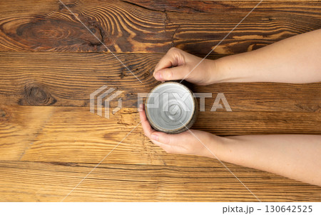 Hand Holds Cup, Empty Cup in Hands, Coffee Mug, Teacup Mockup, Cup in Arms on Wooden Table 130642525