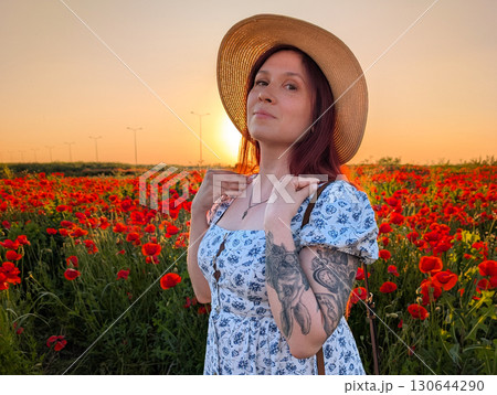 A woman smiles in a straw hat surrounded by red poppies at sunset. Lifestyle, beauty, and natural harmony of rural landscape with human presence and joy. A woman smiles in a straw hat surrounded by red poppies at sunset. Lifestyle, beauty, and natural harmony of rural landscape with human presence and joy. 130644290