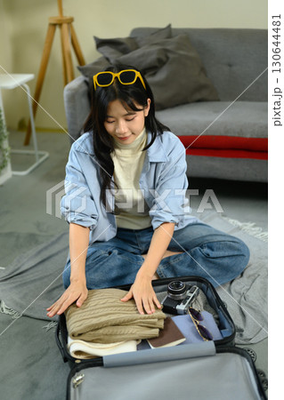 Young woman packing suitcase with clothe and travel essentials, preparing for a trip Young woman packing suitcase with clothe and travel essentials, preparing for a trip 130644481