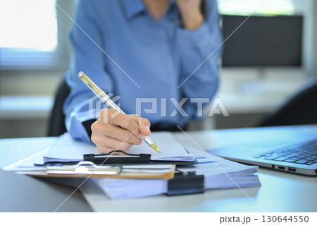 Close up of businesswoman writing on documents while talking on mobile phone Close up of businesswoman writing on documents while talking on mobile phone 130644550