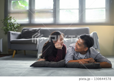 Happy couple lying on the floor with pillows, smiling and looking at each other lovingly at home Happy couple lying on the floor with pillows, smiling and looking at each other lovingly at home 130644578