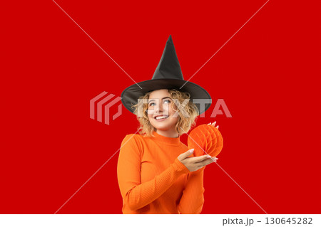 Young woman in a witch hat and orange sweater holds decor 130645282