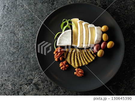 Camembert cream cheese with olives, rosemary, and walnuts on a black plate. Camembert cream cheese with olives, rosemary, and walnuts on a black plate. 130645390