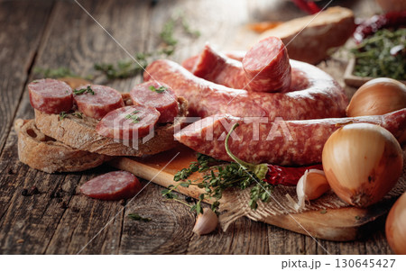 Dry-cured sausage with bread and spices on a old wooden table. Dry-cured sausage with bread and spices on a old wooden table. 130645427
