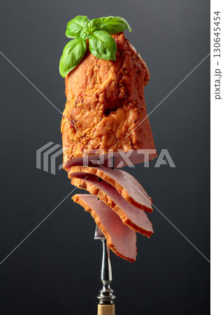 Smoked ham with basil on a fork. 130645454